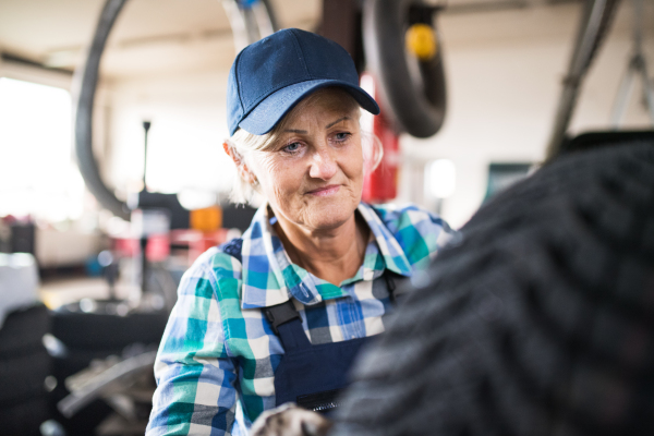 Female mechanic repairing a car. A senior woman working in a garage.