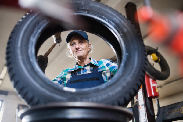 Female mechanic repairing a car. A senior woman working in a garage.