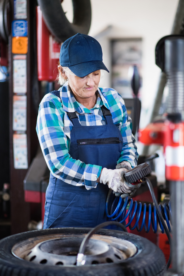 Female mechanic repairing a car. A senior woman working in a garage.