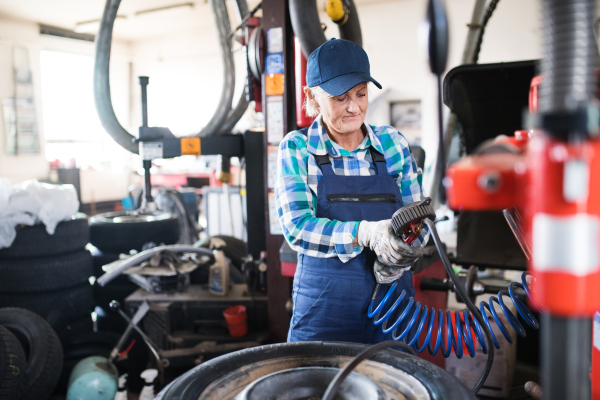 Female mechanic repairing a car. A senior woman working in a garage.