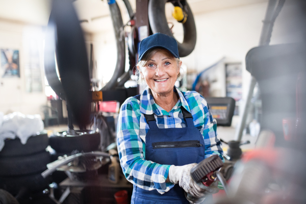 Female mechanic repairing a car. A senior woman working in a garage.