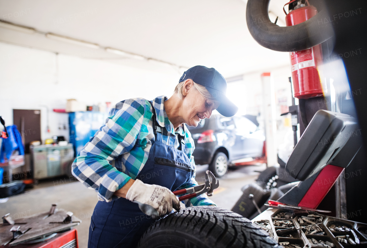 Female mechanic repairing a car. A senior woman working in a garage.