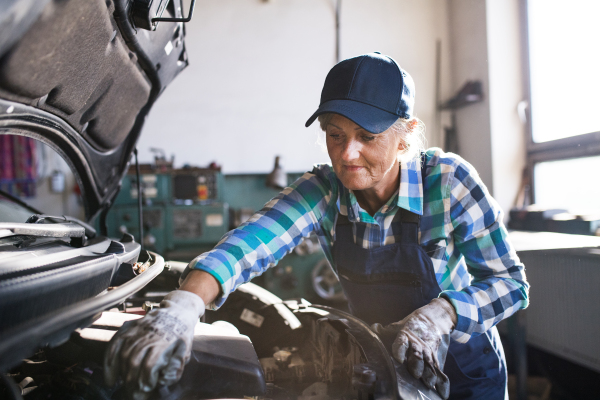 Female mechanic repairing a car. A senior woman working in a garage.