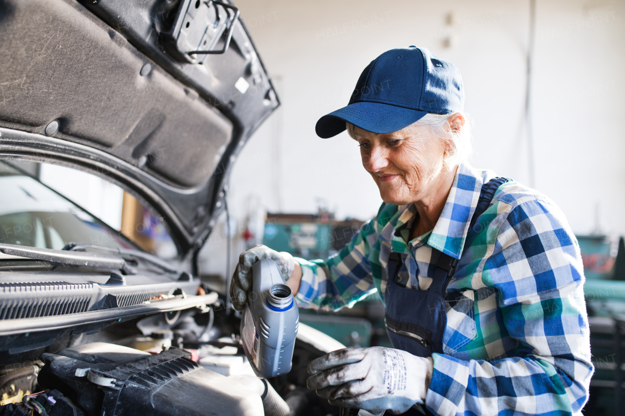 Senior female mechanic repairing a car. A senior woman working in a garage.