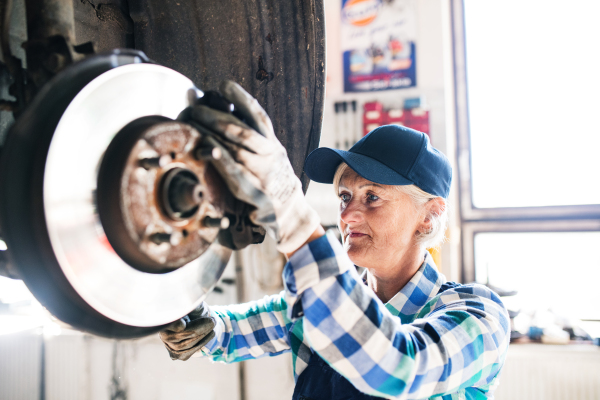 Female mechanic repairing a car. A senior woman working in a garage.