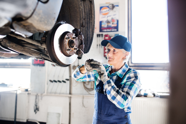 Female mechanic repairing a car. A senior woman working in a garage.