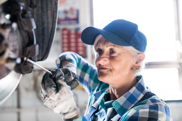 Female mechanic repairing a car. A senior woman working in a garage.