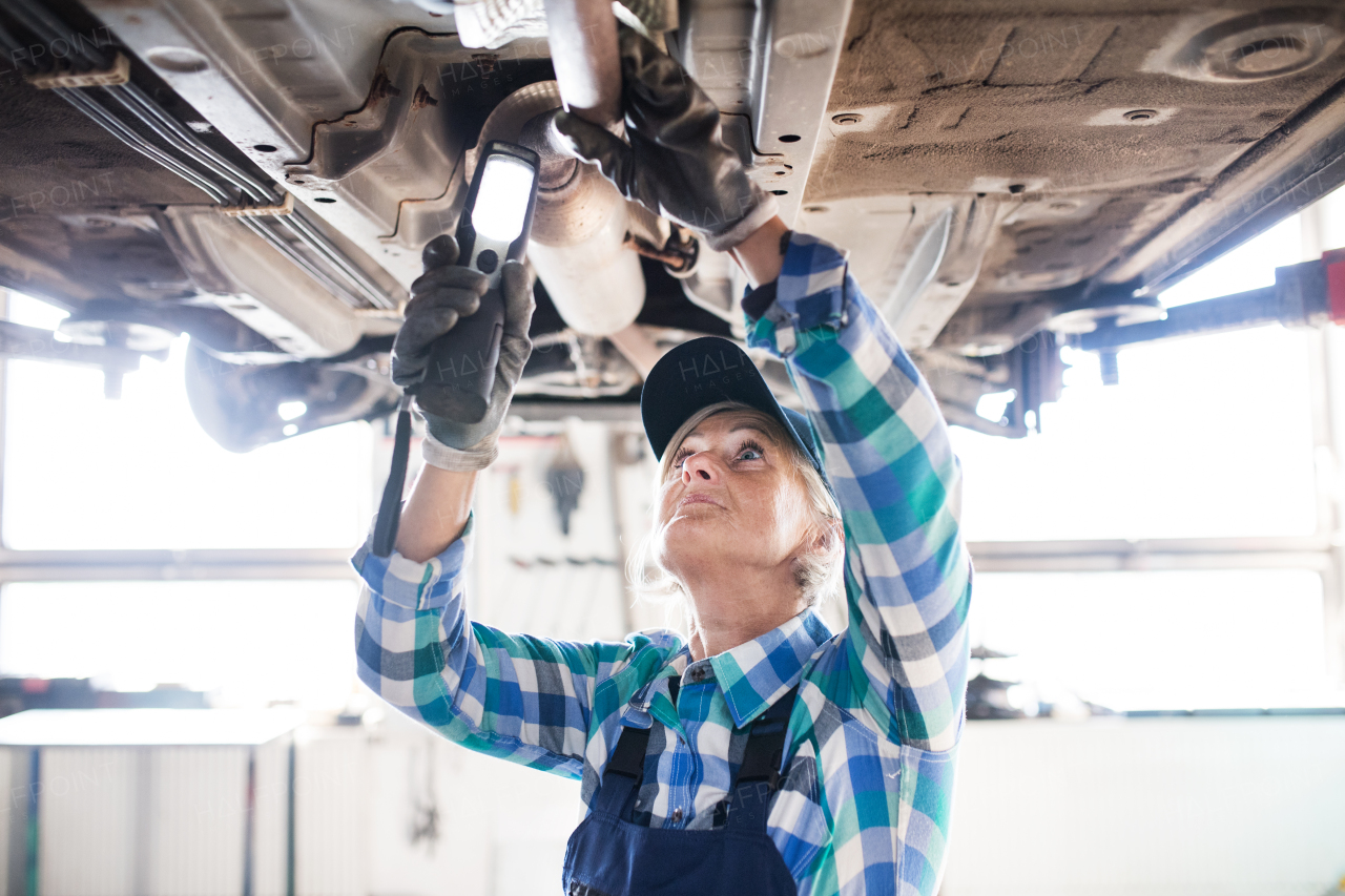 Female mechanic repairing a car. A senior woman working in a garage.