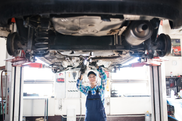 Female mechanic repairing a car. A senior woman working in a garage.