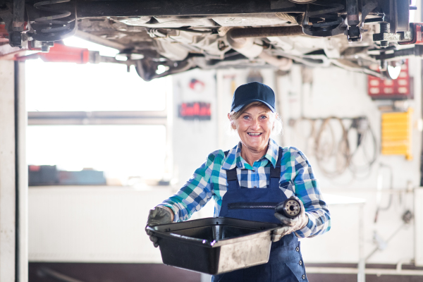 Female mechanic repairing a car. A senior woman working in a garage.