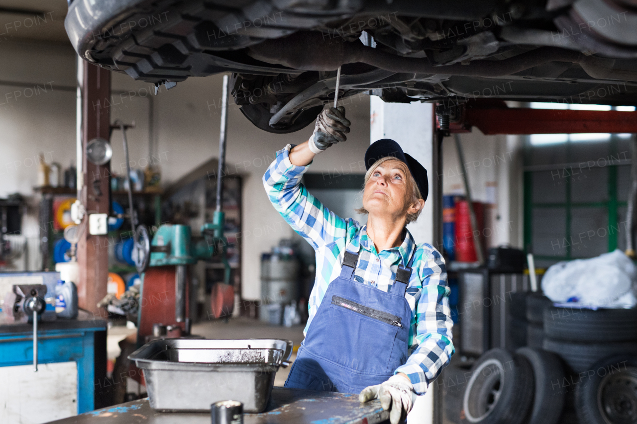 Female mechanic repairing a car. A senior woman working in a garage.