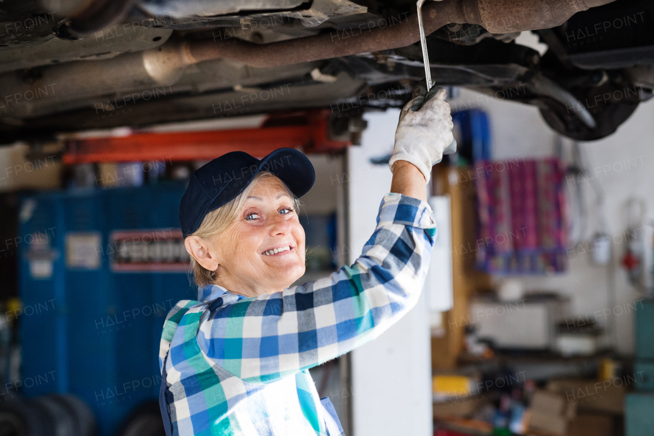 Female mechanic repairing a car. A senior woman working in a garage.