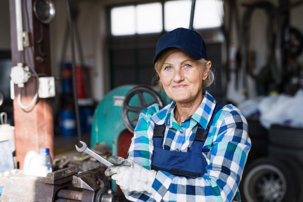 Female mechanic repairing a car. A senior woman standing in a garage.