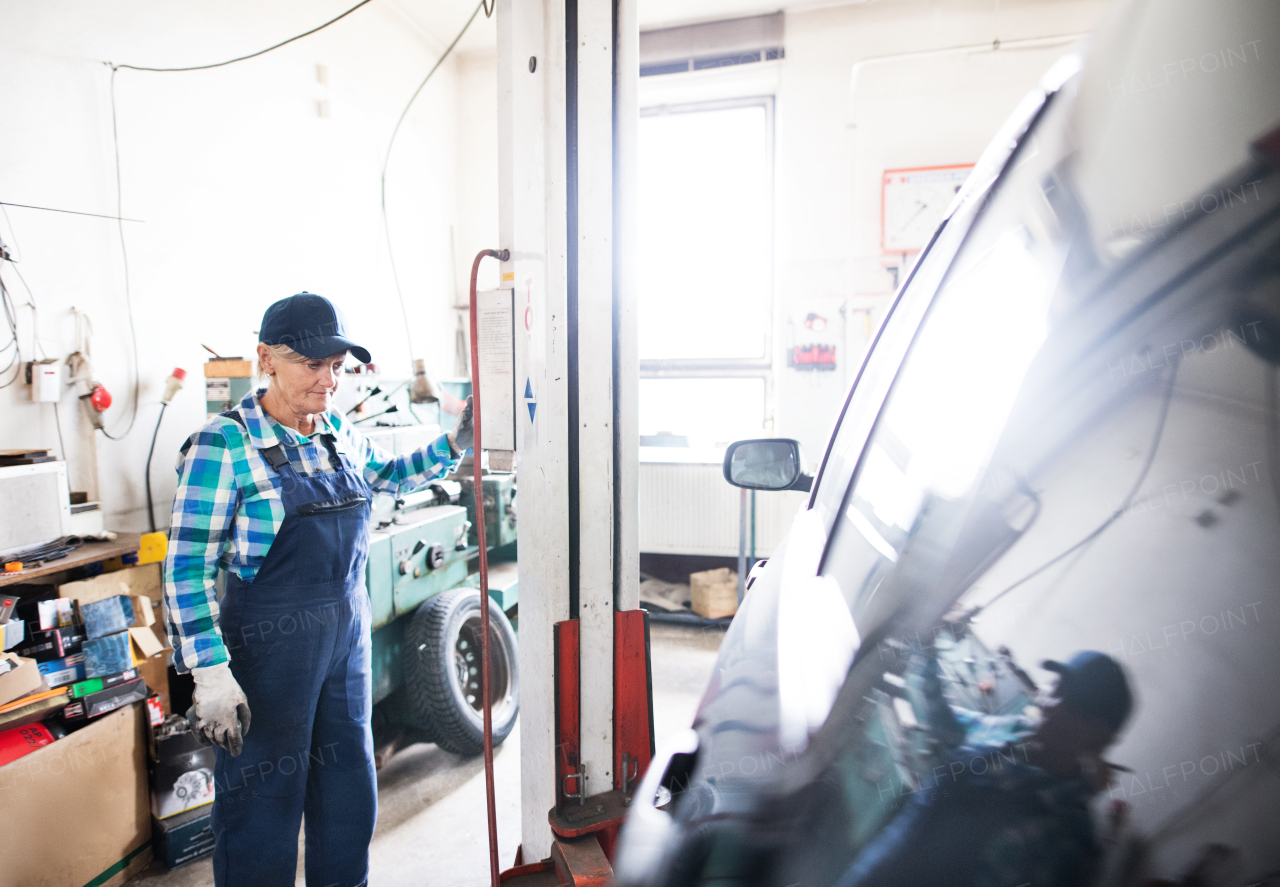 Female mechanic repairing a car. A senior woman standing in a garage.