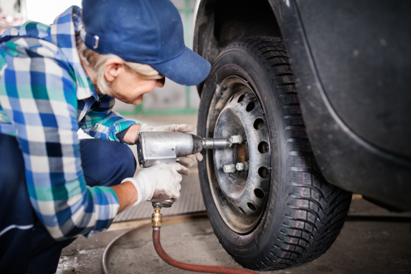 Female mechanic repairing a car. A senior woman working in a garage.