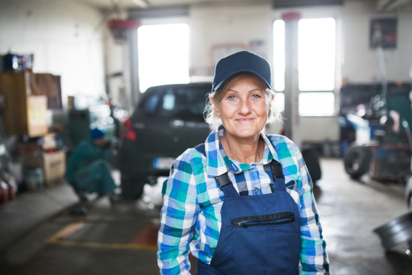 Female mechanic repairing a car. A senior woman standing in a garage.