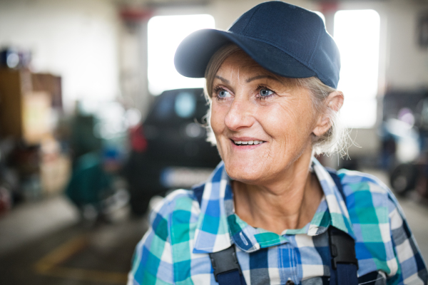 Female mechanic repairing a car. A senior woman standing in a garage.