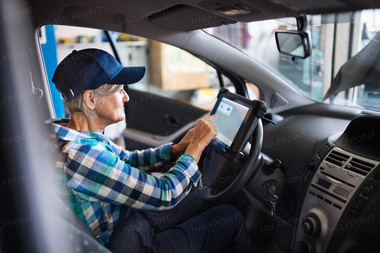 Female mechanic repairing a car. A senior woman working in a garage.