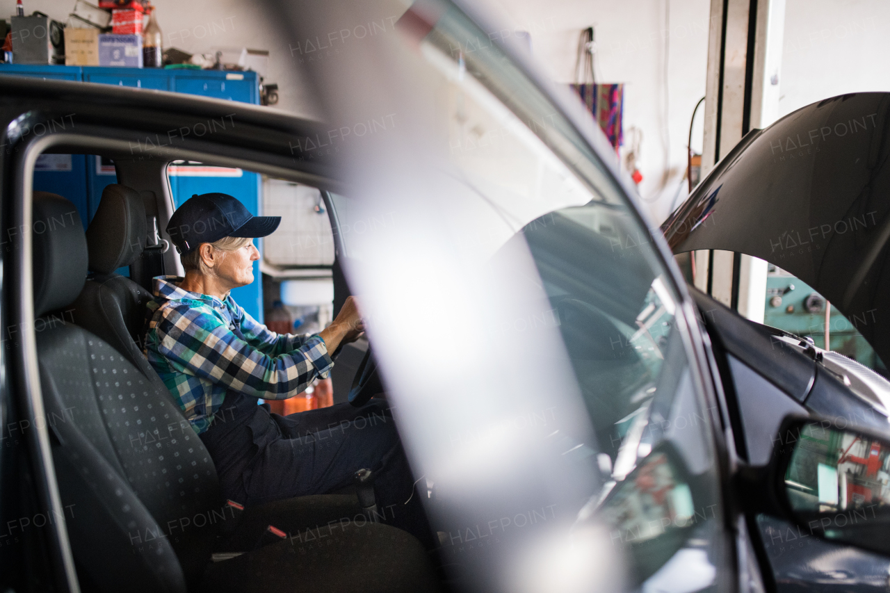 Female mechanic repairing a car. A senior woman working in a garage.