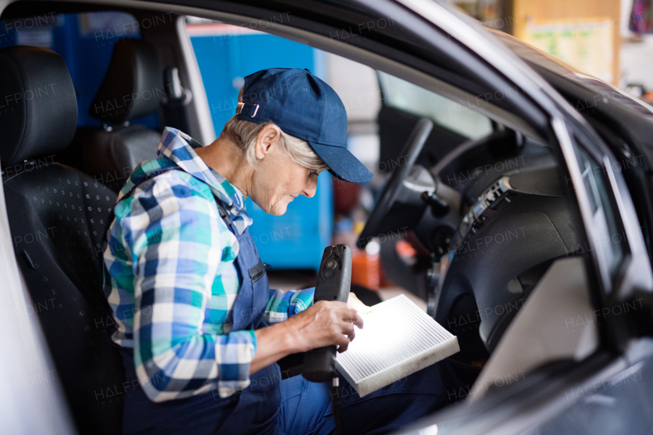 Female mechanic repairing a car. A senior woman working in a garage.