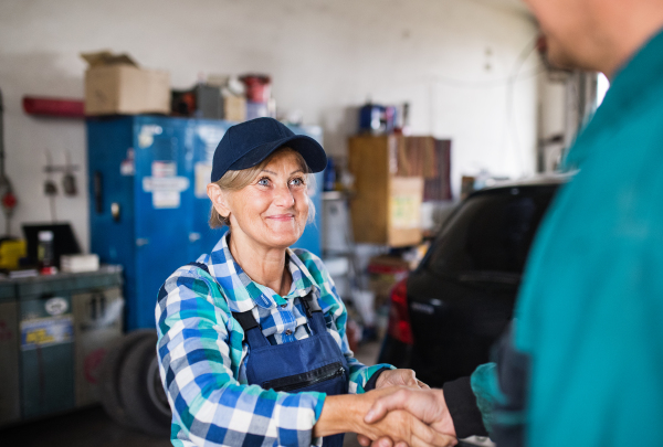 Female mechanic repairing a car. A senior woman shaking hands with an unrecognizable customer.