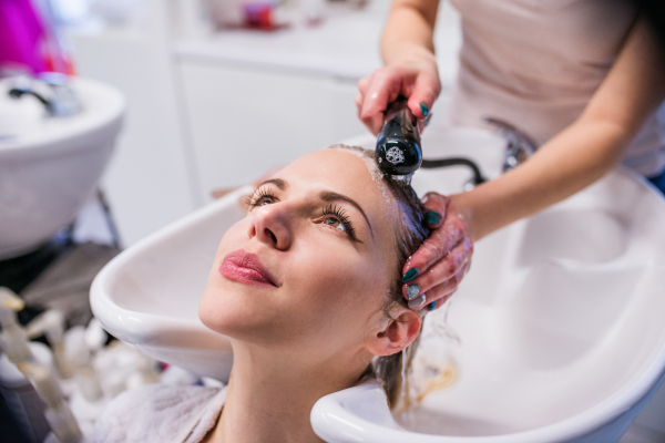 Unrecognizable professional hairdresser washing hair to her beautiful client. Young woman in a hair salon