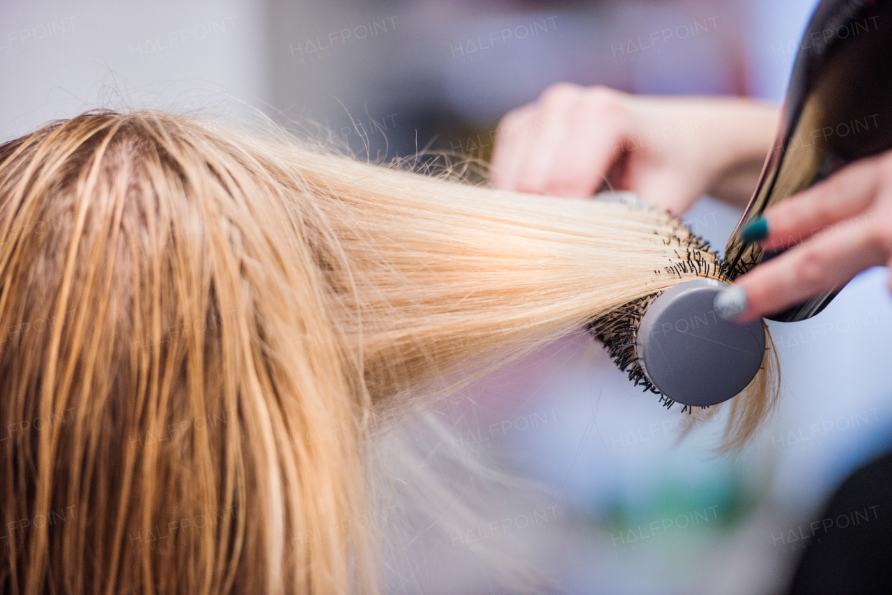 Hands of unrecognizable professional hairdresser drying hair of her client, new haircut, blonde female customer.