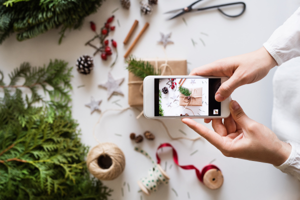 Christmas composition on a white background. Flat lay. Female hands holding a smartphone, taking a photograph.