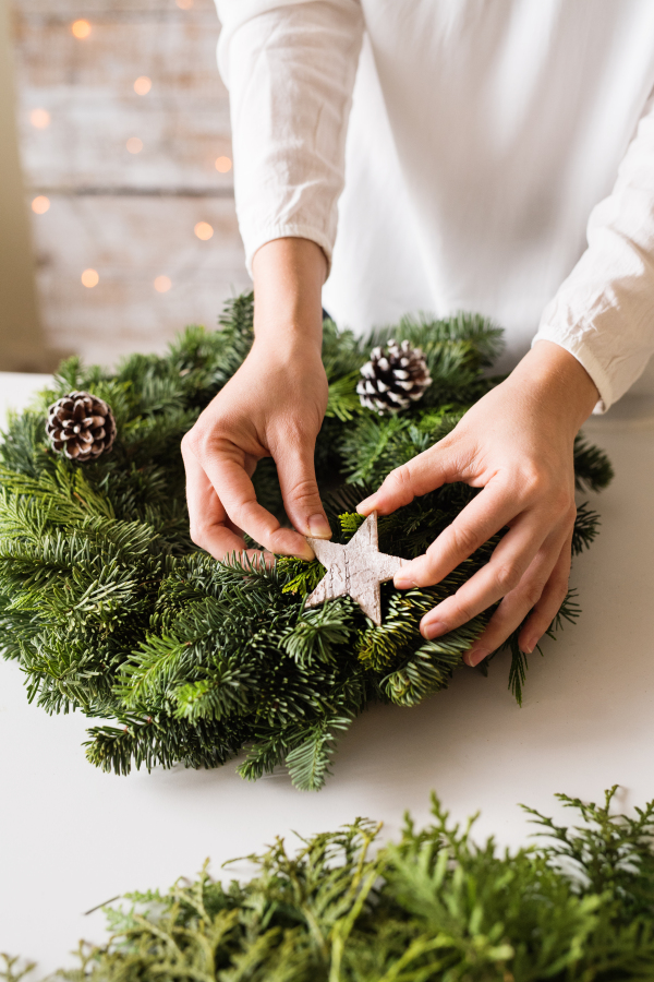 Female hands of unrecognizable woman decorating a wreath. Christmas composition.