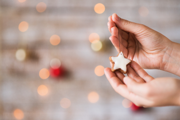 Female hand holding Christmas decorations. A star-shaped biscuit on a string. Copy space.