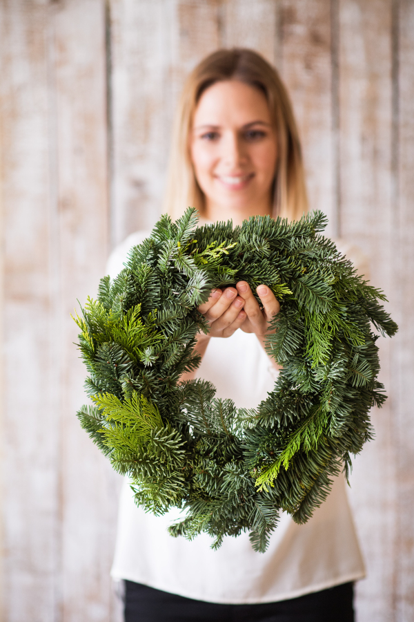 Young woman holding green wreath against wooden background. Christmas composition.