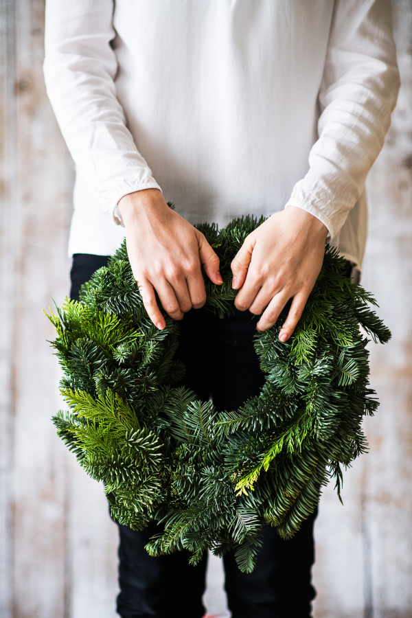 Unrecognizable woman holding green wreath. Christmas composition. Copy space.