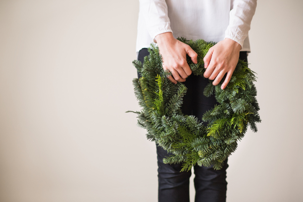 Unrecognizable woman holding green wreath. Christmas composition. Copy space.