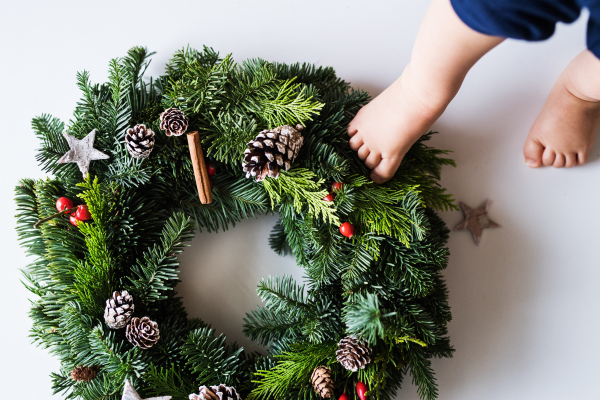 Feet of a baby stepping on christmas wreath on a white background. Top view.