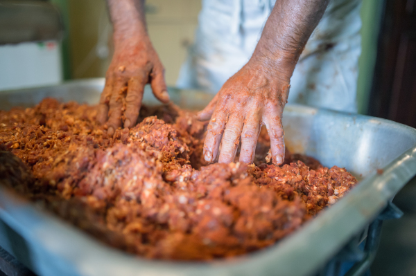 Unrecognizable man making sausages the traditional way at home. Mixing meat and spices in the bowl.