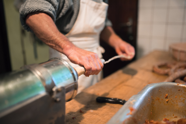 Unrecognizable man making sausages the traditional way using sausage filler. Homemade sausage.