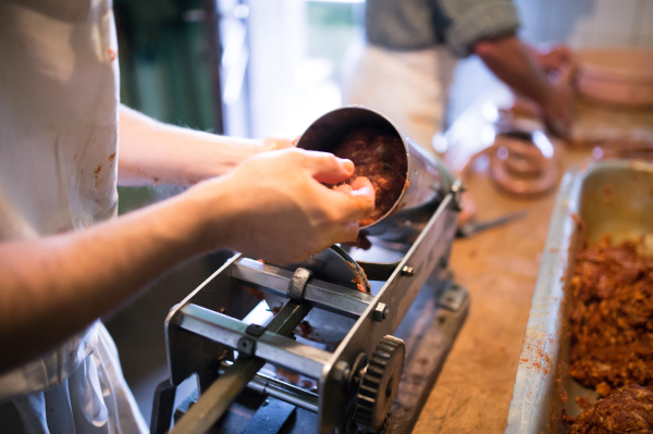 Unrecognizable man making sausages the traditional way at home. Putting meat ball into sausage filler. Close up.