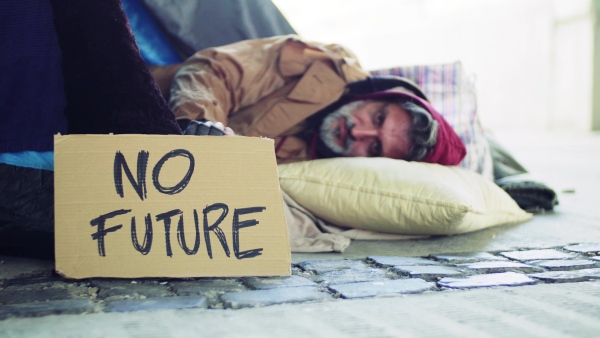 Homeless beggar man lying outdoors in city in a sleeping bag, no future cardboard sign near him.