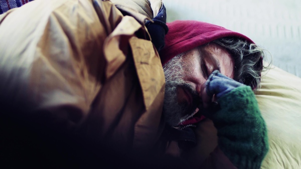 A close-up portrait of homeless dirty beggar man lying outdoors.