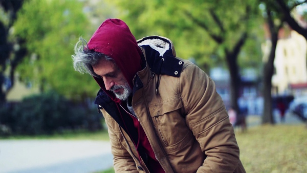 A portrait of homeless beggar man outdoors in park in autumn.