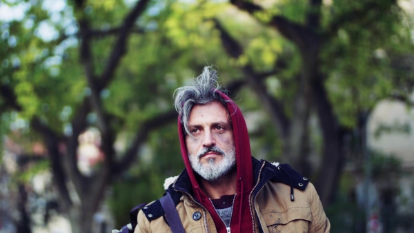 A portrait of homeless beggar man walking outdoors in park in autumn.