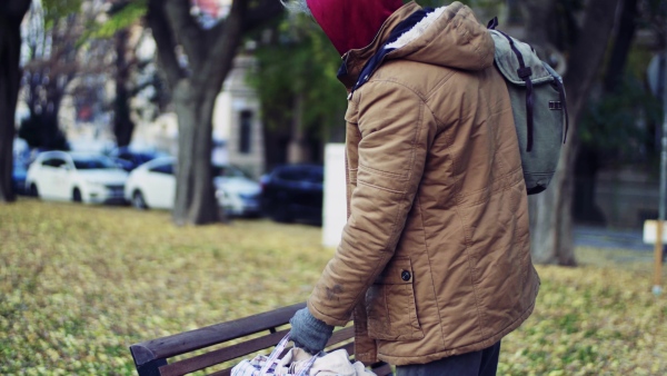 A portrait of homeless beggar man walking outdoors in park in autumn.