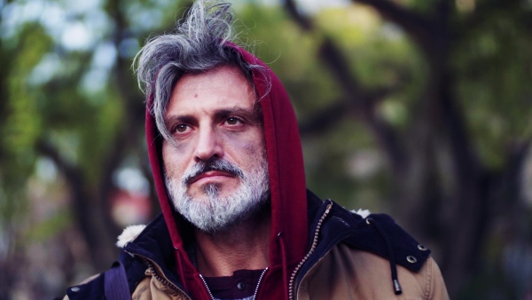 A portrait of homeless beggar man walking outdoors in park in autumn.