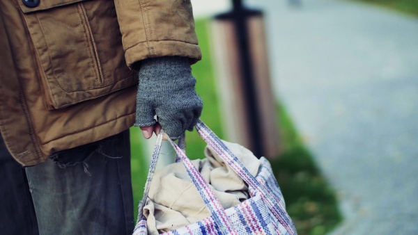 A midsection of portrait of homeless beggar man walking outdoors in park in autumn, carrying a bag.