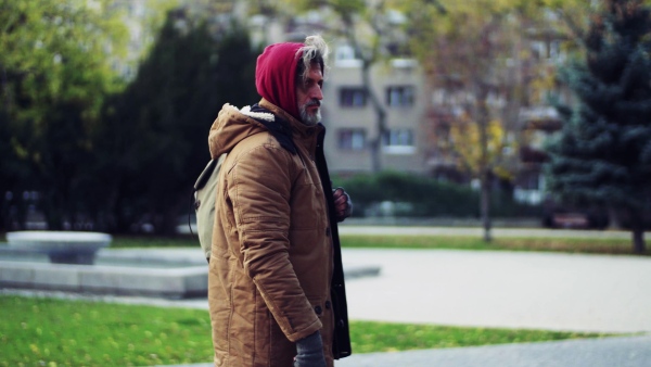 A portrait of homeless beggar man walking outdoors in park in autumn.