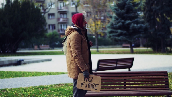 A portrait of homeless beggar man walking outdoors in park in autumn.