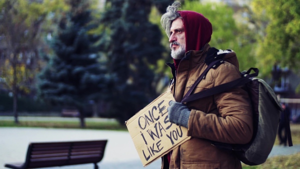 A portrait of homeless beggar man walking outdoors in park in autumn.