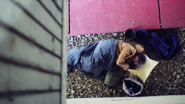 A top view of homeless beggar man lying on the ground outdoors in city in a sleeping bag, asking for money donation.