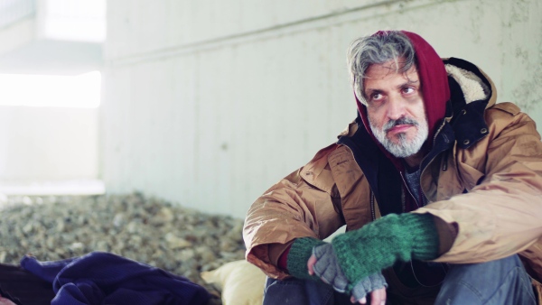 A portrait of homeless dirty beggar man sitting outdoors.