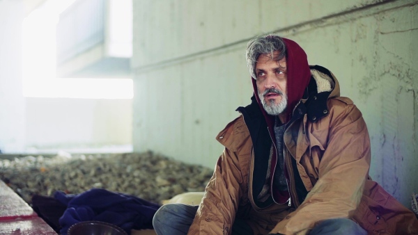 A portrait of tired homeless dirty beggar man sitting outdoors. Slow motion.